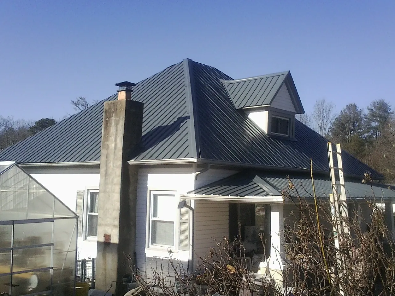 Dark blue standing seam metal roof on a white farmhouse with dormer — Slate & Tile Roof Repair by Roofing Brothers in Red Lodge