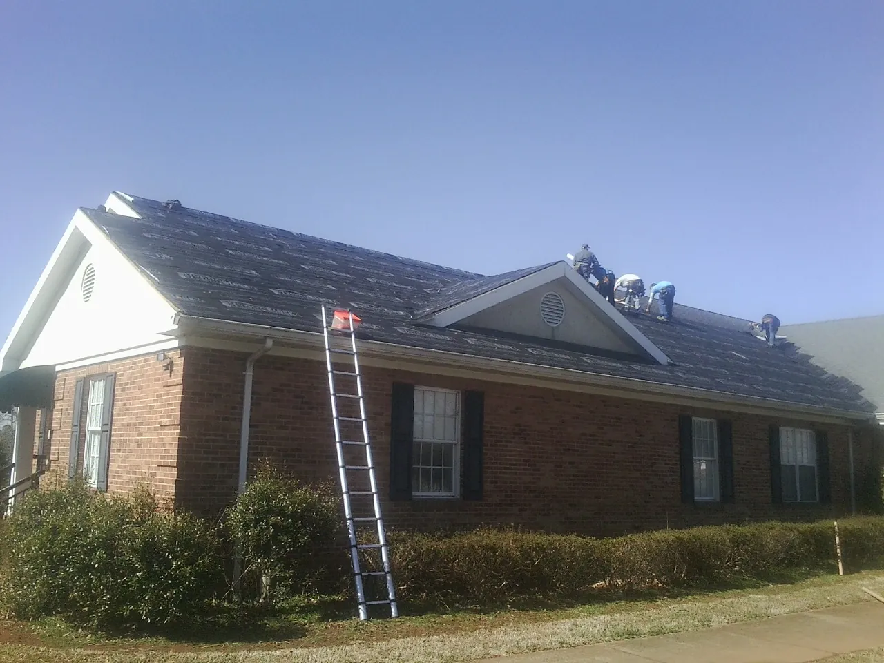 Crew tearing shingles off a brick ranch roof with a ladder set — Emergency Roof Repair work by our crew in Red Lodge