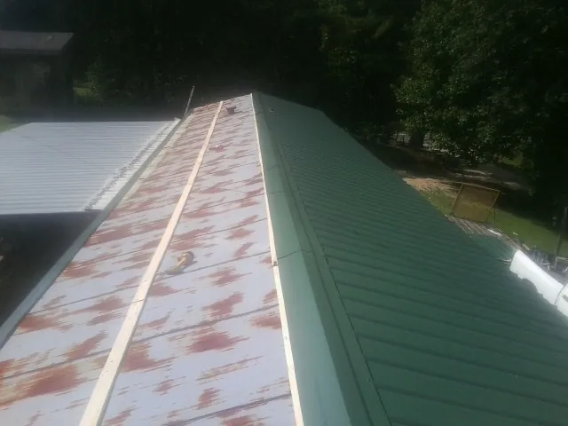 Old rusted panels beside newly installed green metal roofing — Wind Damage Roof Repair by Roofing Brothers in Red Lodge