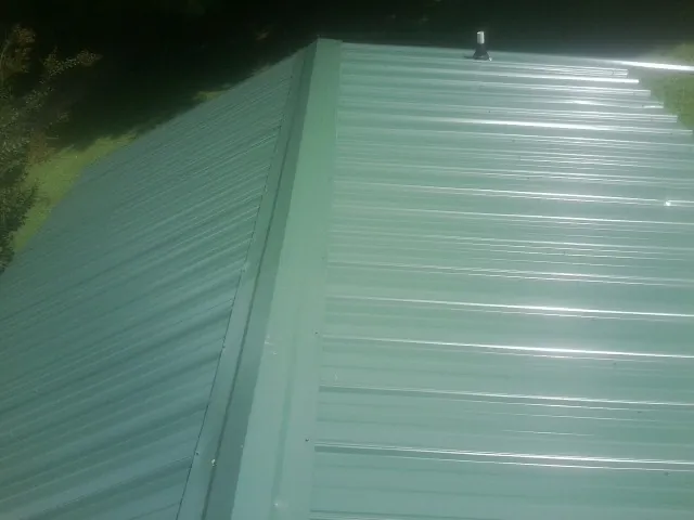 New green metal panels meeting at the ridge of a roof — Flat Roof Repair work by our crew in Red Lodge