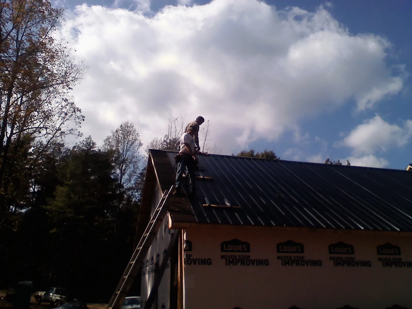Roofer fastening dark metal panels high against a cloudy sky, from a Roof Inspection job in Red Lodge