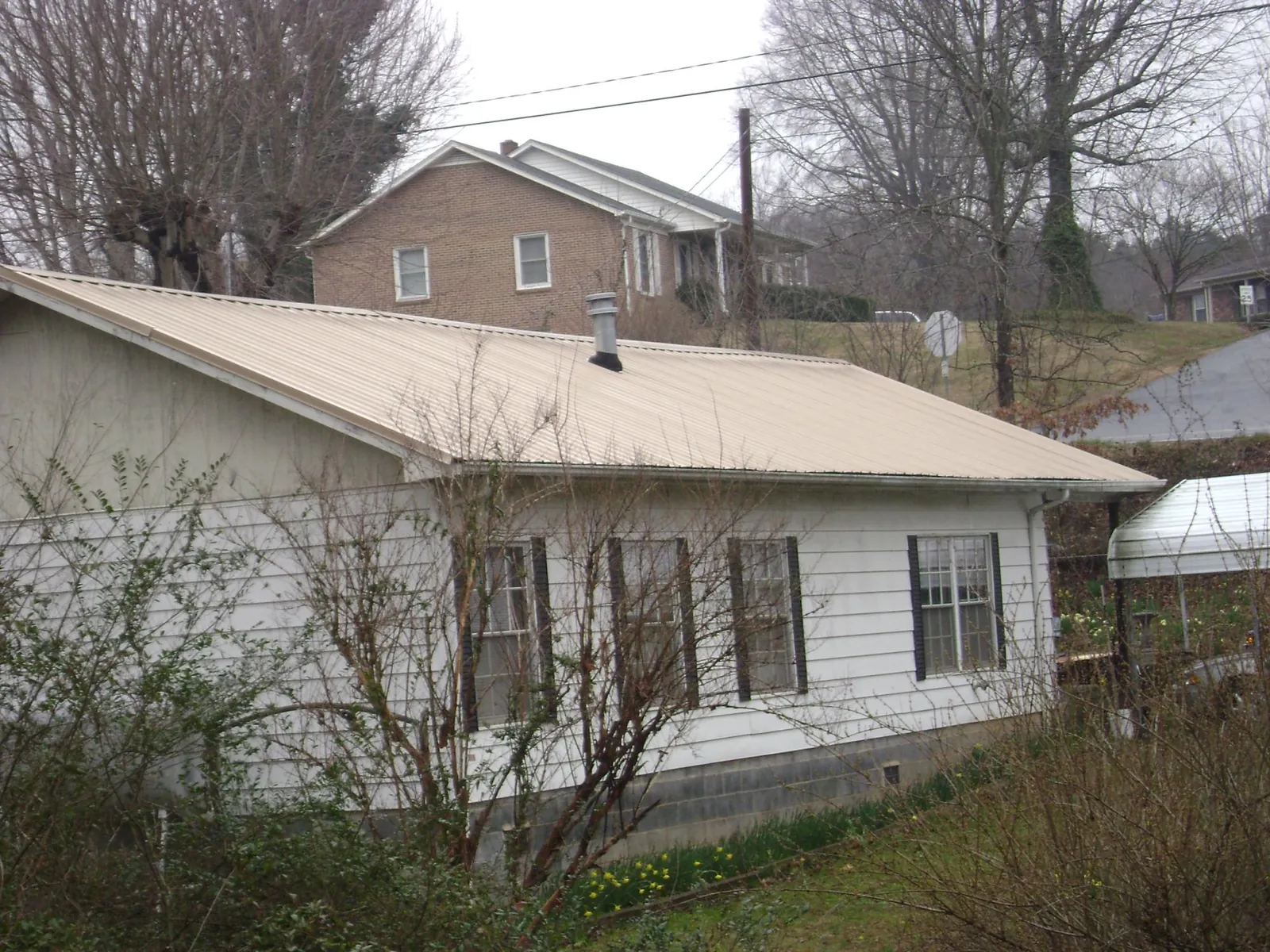 Tan metal roof on a white sided house set into a hillside — Commercial Roofing by Roofing Brothers in Red Lodge